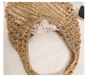 Close-up of golden woven mesh tote bag with beige drawstring lining on white fabric