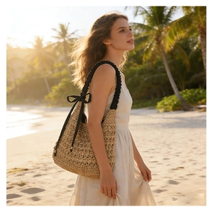 Détail du sac en paille avec bandoulière à volants noirs et nœud sur une plage