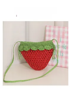 Detailed view of handmade strawberry woven bag featuring green tassels and red crochet texture
