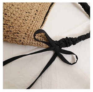 Gros plan sur le nœud noir et la texture en paille de ce sac à bandoulière de plage