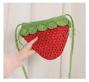 Detail of red strawberry straw bag with green leaf flap and woven shoulder strap