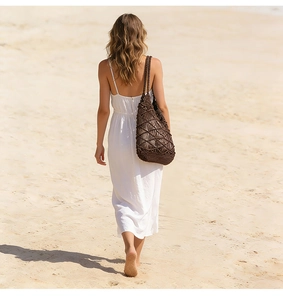 Detail of dark brown lattice woven beach bag shown with a white summer dress on sand