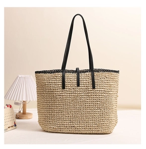Detail der gewebten Stroh-Tote-Bag mit schwarzen PU-Lederriemen auf einem weißen Tisch