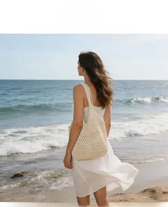 Chic beige crochet shoulder bag shown on model with a white dress at the beach