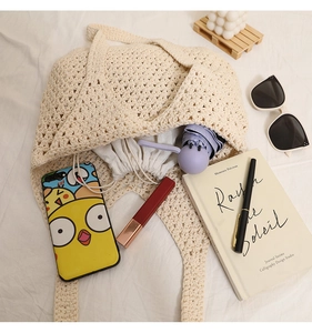 Flat lay of cream hollow-out crochet tote bag with sunglasses and books for beach vacation