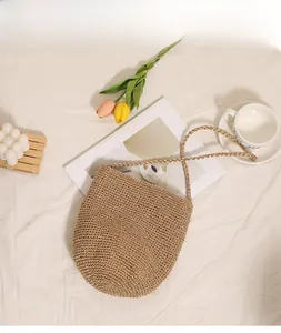 Detail view of a woven straw bucket bag with long strap on a white fabric surface