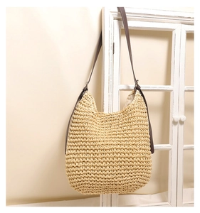 Hobo straw bag with brown PU strap hanging on a vintage wooden window frame