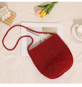 Close-up of red hand-woven bucket bag with cylindrical base and woven strap on white fabric