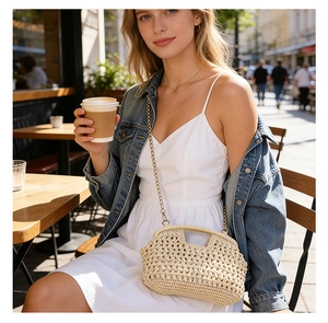 Detail of hollow-out beige straw bag with metallic chain strap in outdoor cafe setting