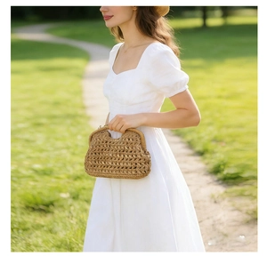 Detail of light brown woven straw clutch bag with unique curved handle on a sunny lawn