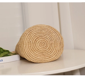 Detailed macro view of the circular spiral woven base of a raffia straw bucket bag