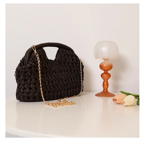 Detail of dark brown hand-woven straw bag with metal chain strap and round top handle