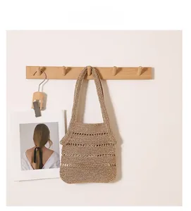 Close-up of a handmade hollow-out straw tote bag hanging on a minimalist wooden hook