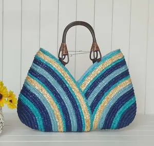 Detail of multi-color blue woven straw tote bag with brown handles on white wood surface