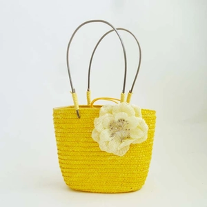 Detailed view of yellow woven straw bag with cream mesh flower and metal handles