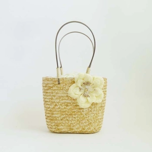 Close-up of woven straw bag with floral decoration and round metal handles
