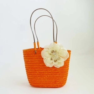 Detail of orange hand-woven straw bag with white floral accent for beach vacations