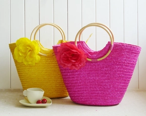 Detail of colorful straw bags with large satin flowers and round wooden handles for beach