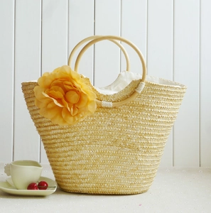 Detail of hand-woven straw beach bag with large yellow flower and round wooden handle