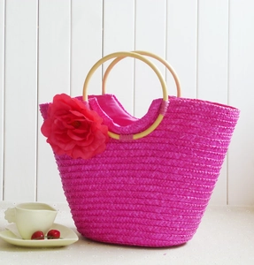 Macro detail of handwoven straw bag with vibrant red flower and round wooden handle