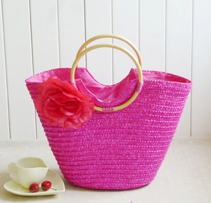 Detail of rose pink woven straw bag featuring a large flower and wooden round handles