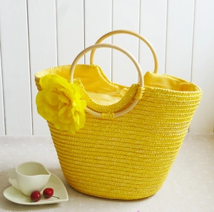 Detail of yellow straw beach bag featuring a large fabric flower and round wooden handle