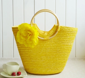 Macro detail of a bright yellow woven straw tote bag with floral decor and wooden handles