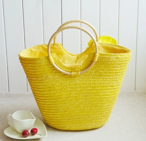 Detail of yellow straw tote bag featuring wood round handles and floral ornament