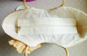 Internal view of straw beach bag with fabric lining, zipper closure, and wooden handles