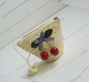Detail of straw woven crossbody bag with cherry decor and black and white bow