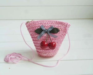 Close-up of pink straw bag featuring cherry ornaments and a black checkered bow detail