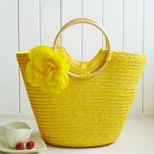 Yellow straw tote bag with large floral decoration and round wooden handles for summer beach