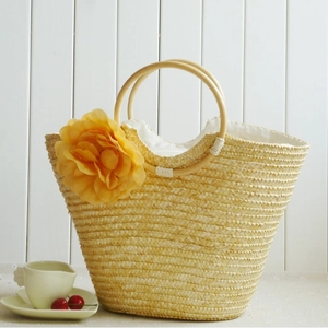 Straw beach bag with yellow flower and wooden handles on white wooden fence background