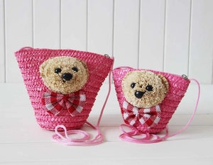 Detail of two fuchsia straw bags featuring plush teddy bear heads and zipper closure
