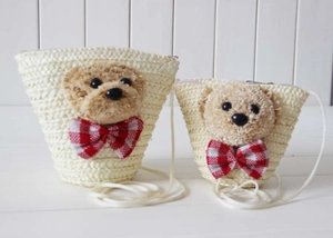 Detail of hand-woven straw crossbody bag with plush bear head and red plaid bow