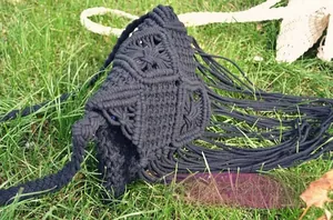 Close-up of black handmade macrame shoulder bag with long bohemian fringe on grass