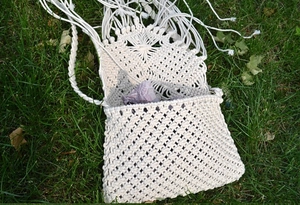 Detail of handmade macrame bag with long tassels on grass for beach vacation style