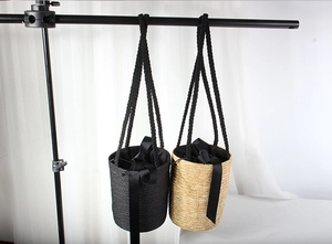 Detail of hand-woven straw bucket bag with black ribbon bow and braided shoulder strap