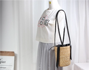Detail of woven straw bucket bag with black bow and shoulder strap on model