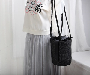 Detail of a black woven straw bucket bag with ribbon bow on a female model shoulder