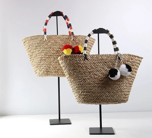 Detail view of woven straw tote bags with colorful pom-pom charms and striped handles