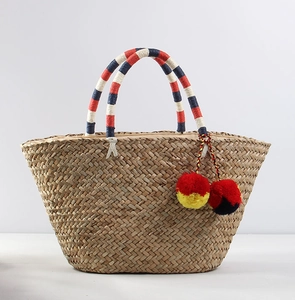 Detail of bohemian straw tote featuring colorful pom-poms and woven handle accents