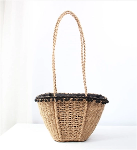 Detail of straw woven tote bag featuring black pom pom trim and long shoulder straps