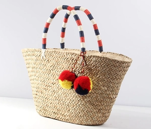 Close-up of woven straw tote bag with colorful tassel pom-poms and multicolor handles
