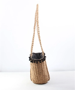 Detail of straw bucket bag with black pom-pom trim and woven shoulder strap