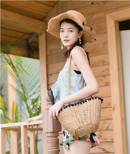 Detail view of a beige straw shoulder bag with black pom-pom trim and a matching sun hat