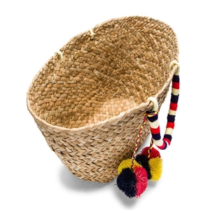 Close-up of woven straw tote bag with colorful cotton wrapped handles and fuzzy pom-poms