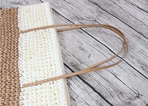 Detail of two-tone woven straw tote bag featuring contrast stitching on slim faux leather straps