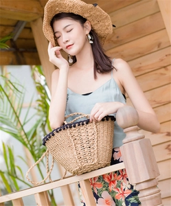 Detail view of a semi-circular straw bag with black pom-pom trim and woven texture