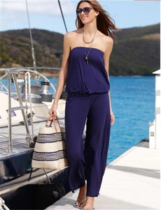 Outdoor shot of a model wearing a navy blue strapless wide-leg jumpsuit on a yacht deck